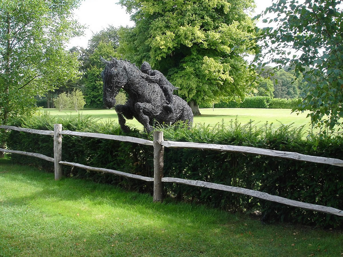 A life-size wire sculpture of a 15.3 hands horse and rider cruising over hedge. In copper wire